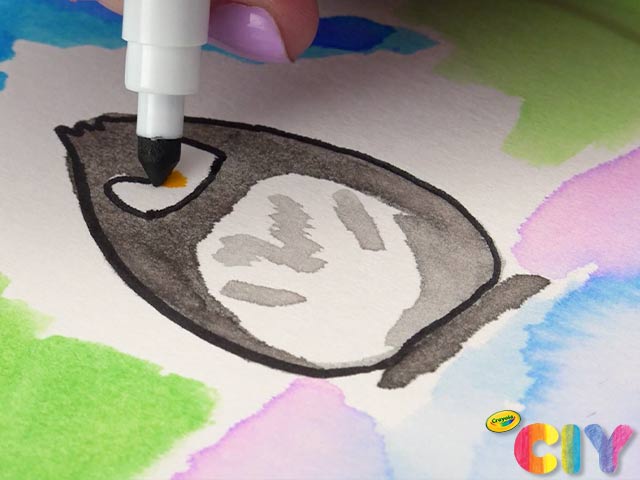 Painted penguin on paper plate being outlined and decorated with Crayola Marker 