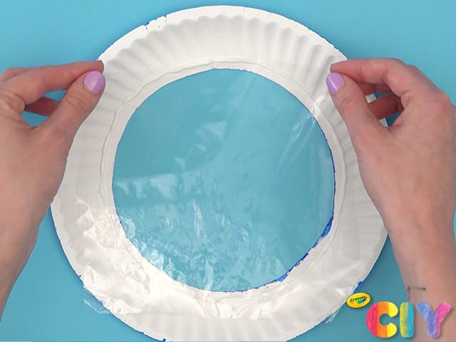 Hands attaching plastic wrap to back of paper plate ring with center cut out 