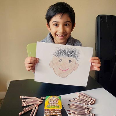 Boy holding up drawn self-portrait using Colors of the World Crayons