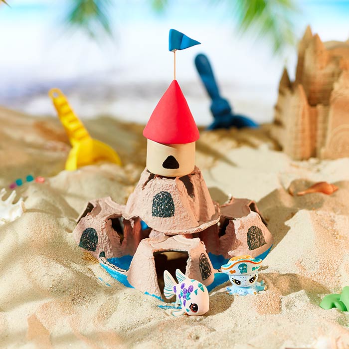 upcycled cup carrier sandcastle craft. craft placed in beach scene surrounded by scribble scrubbies pets.