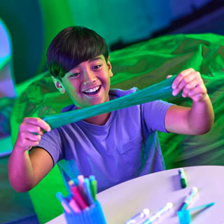 Young boy stretching green colored Crayola Goo