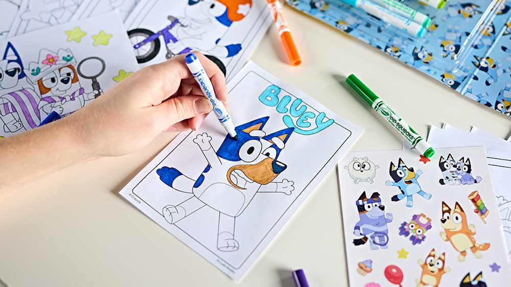 Hand coloring Bluey with Crayola Pop Squeaks markers surrounded by Bluey  pages and stickers.
