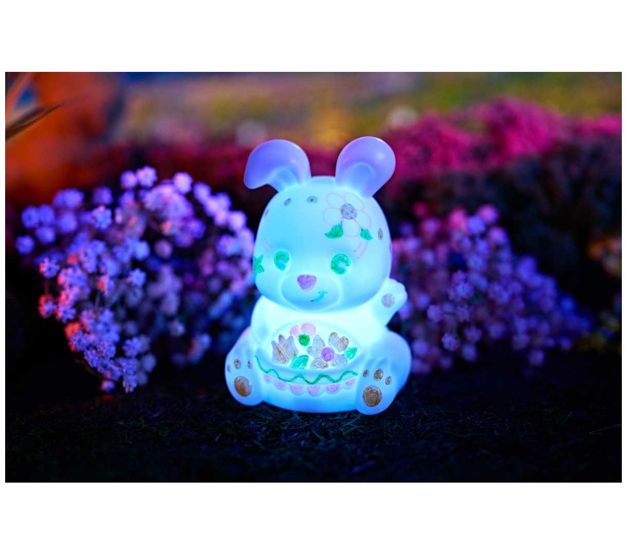 Light-Ups Bunny decorated and glowing blue in front of flowers.