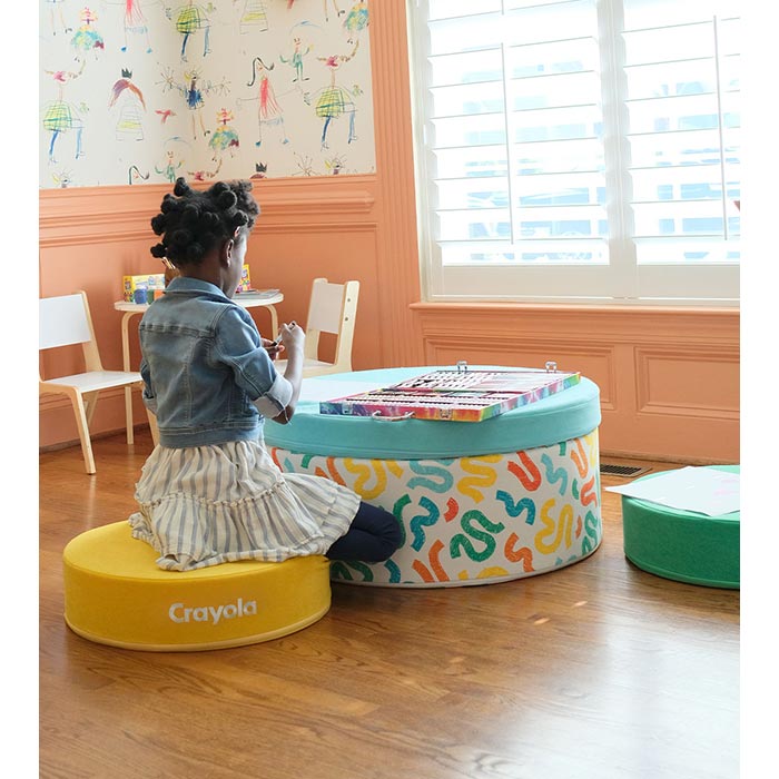 The Crayola Chunk® components with child sitting on a puck and using stacked hoop and pad as a desk.