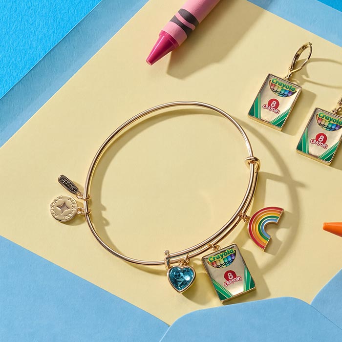 Crayola Teacher Appreciation Multi Charm Bangle. Multi charm bangle and box earrings on yellow paper with scattering of crayons.
