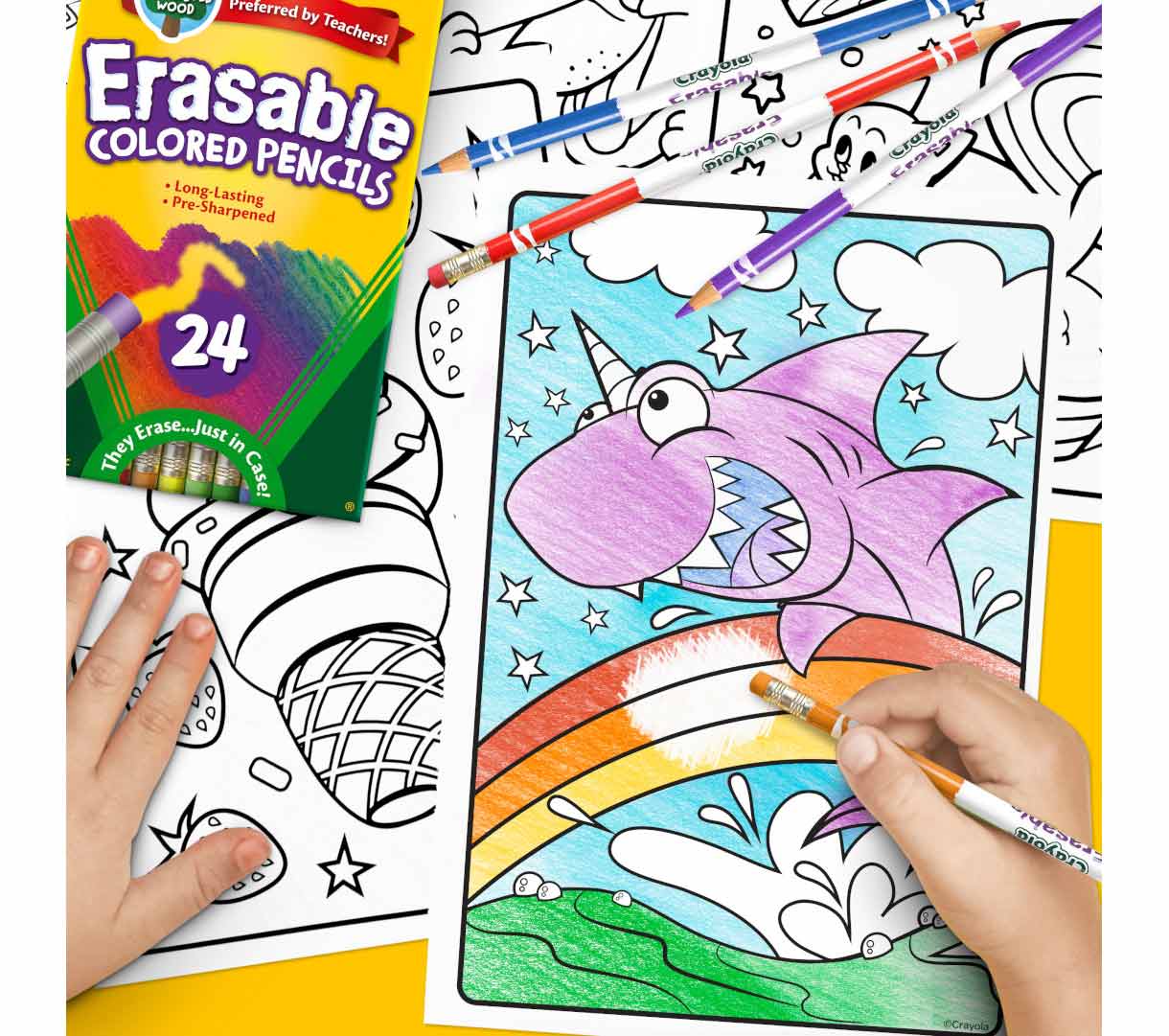 Erasable Colored Pencils  24 count. Hand erasing colored picture of uni-shark. Three additional pencils and box on top of uncolored pages in the background.