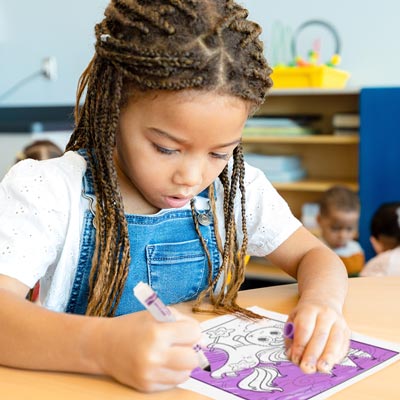 Young girl coloring unicorn coloring page with purple marker